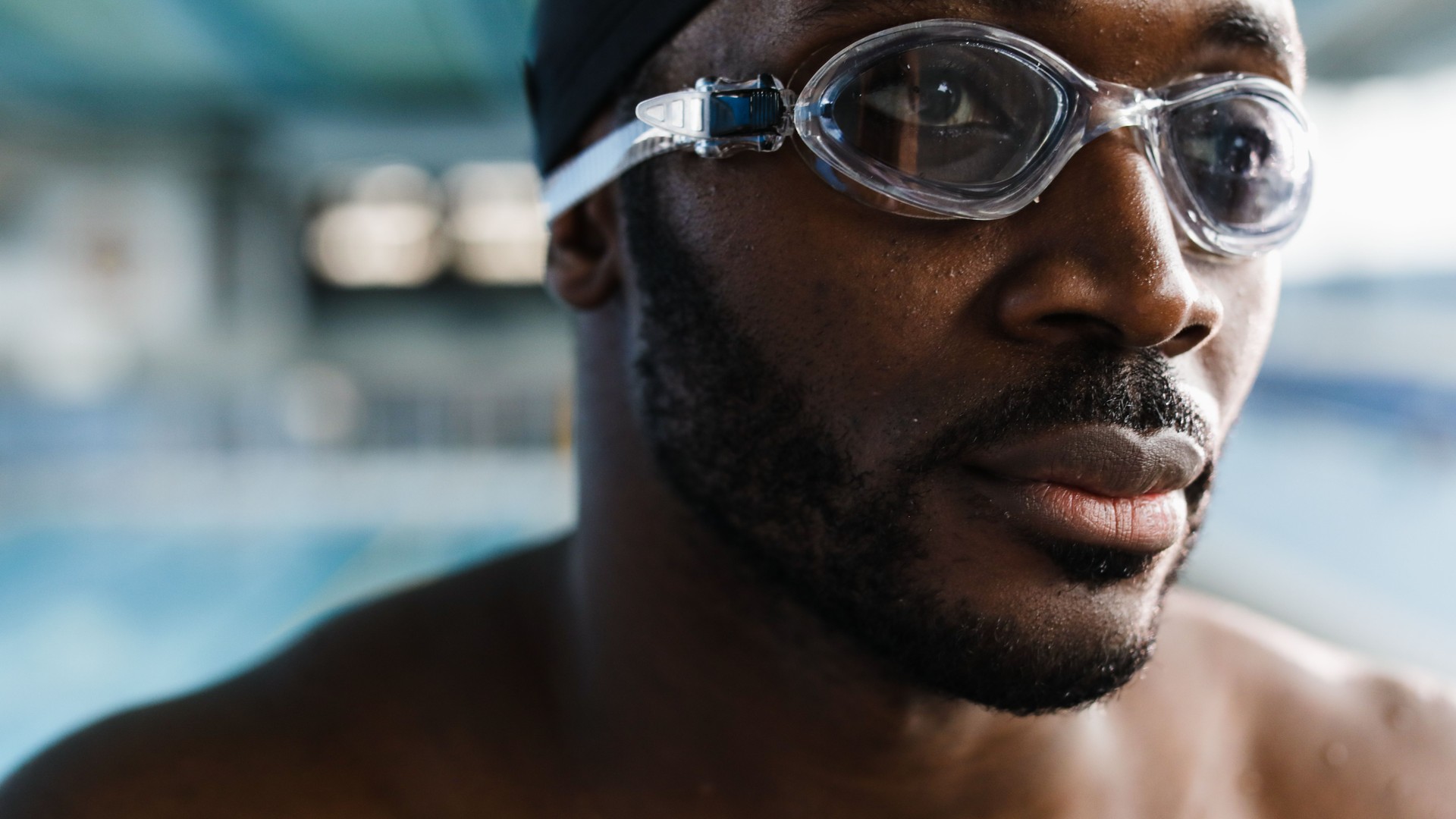 Close-up of a focused male swimmer in goggles at an indoor pool, ready to push off the wall.